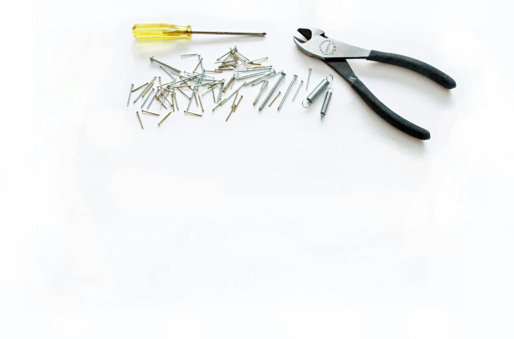 Foto von handwerklichen Werkzeugen und Eisenwaren, darunter einem Schraubenzieher, einem Seitenschneider, Nägeln, Schrauben und Zugfedern